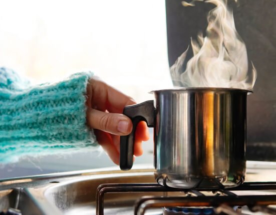 Human hand putting saucepan on gas