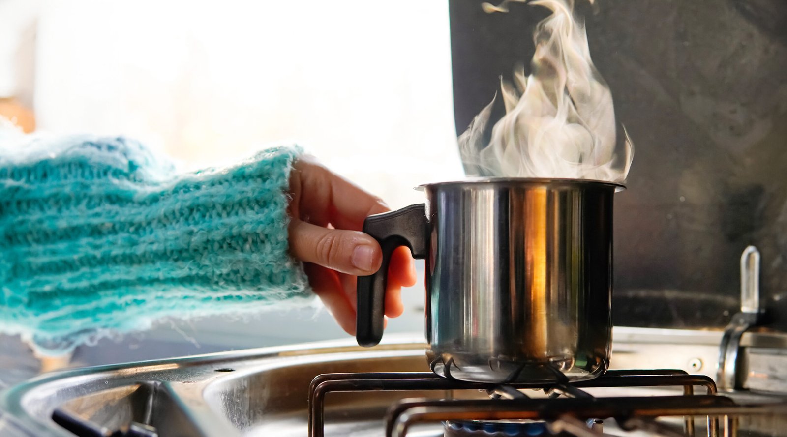Human hand putting saucepan on gas