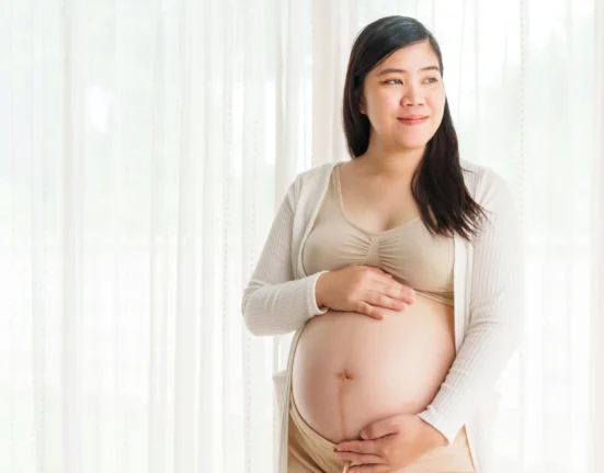 Ibu hamil berdiri sambil memegang perutnya, menunjukkan pentingnya perawatan kulit yang aman selama kehamilan.