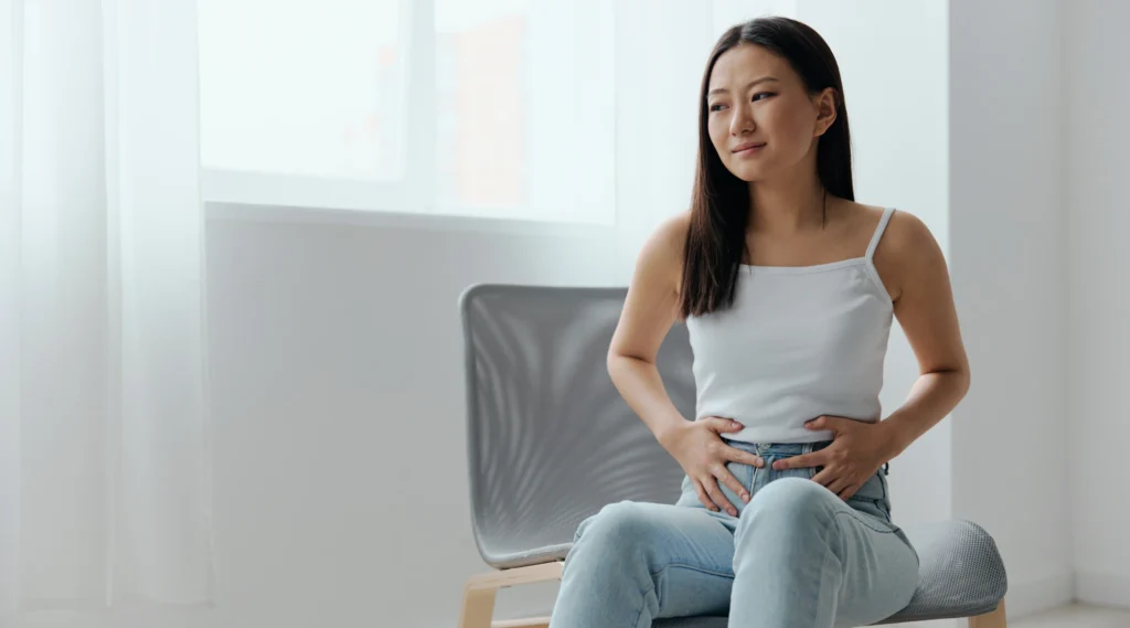 Perempuan duduk sambil memegang perut bagian bawah, mengekspresikan rasa tidak nyaman saat menstruasi yang bisa diperparah oleh keringat berlebih di area intim