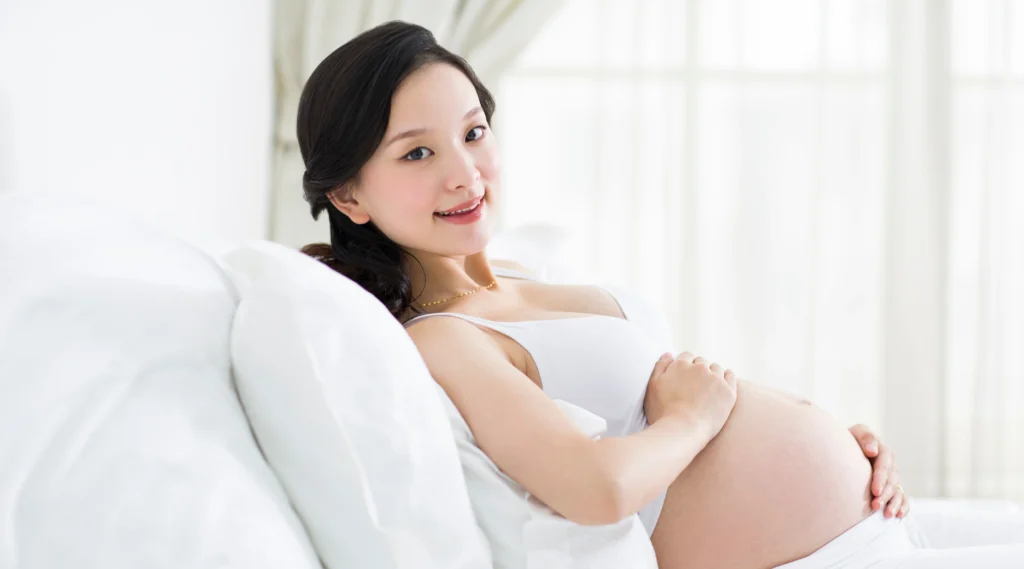 Ibu hamil berbaring santai di tempat tidur, tampak nyaman dan percaya diri dengan pilihan skincare aman untuk kehamilan.