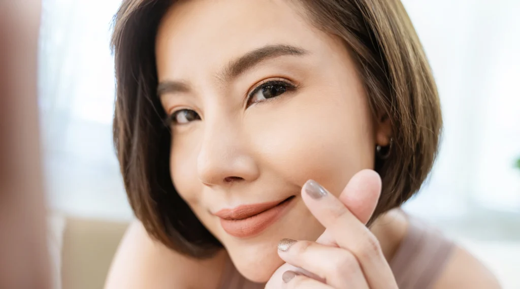 Perempuan dengan kulit wajah halus menunjukkan simbol hati kecil, menandakan kepercayaan diri setelah merawat bekas jerawat